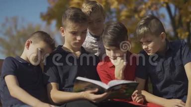 男孩们一<strong>起坐</strong>在长凳上，骑着一本书。 朋友们在秋天的公园里度过一个阳光明媚的日子。